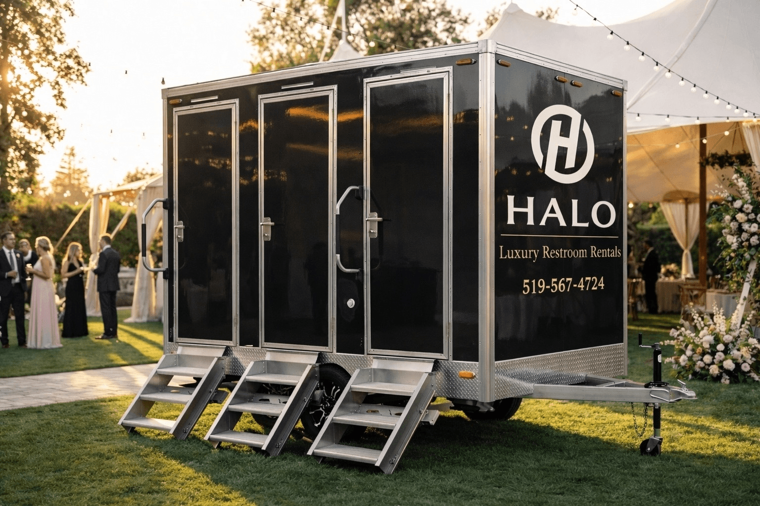 Black Halo luxury restroom trailer with three doors and silver steps at an outdoor wedding event.